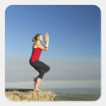 den unga kvinnan övar yoga på en bluff i fyrkantiga klistermärken