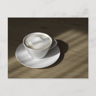 A kopp av cappuccino-kaffe ljuger på en ek vykort
