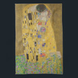 Älskare Kissing Embrace av Gustav Klimt Kökshandduk<br><div class="desc">Solljus blundar från det virvlande guldomfamning som omger älskare i Gustav Klimts mästerverk, The Kiss. Scenen är en paradox med intimitet och isolering. Paret står på en avgrund, en fält av färgstarka blommor på fötterna, men ändå är de omedvetna mot omvärlden. Deras blickar är låsta, deras kroppar är sammanflätade i...</div>