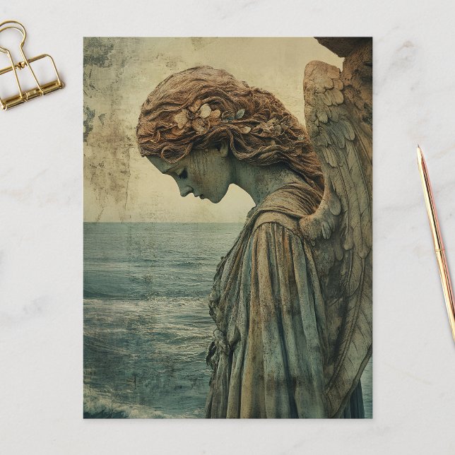 Ängelskulptur med patina vykort (Angel statue covered in patina and distressed on a postcard that is laid on a marble flat surface.)