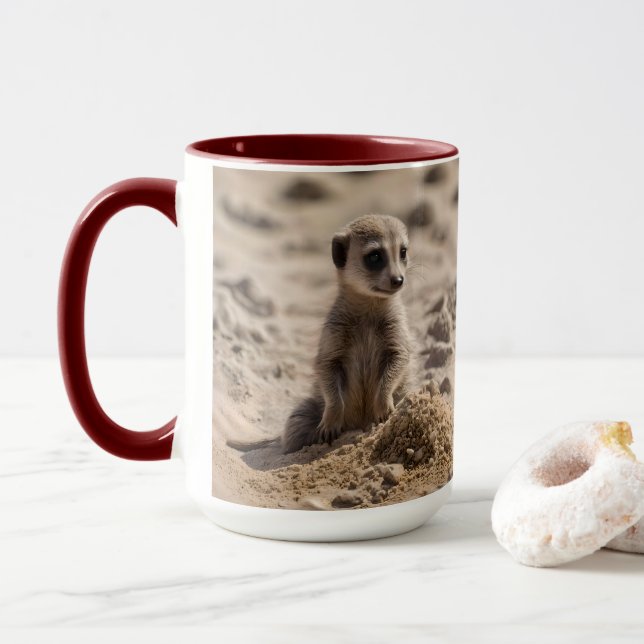 Baby Meerkat spelar i sanden. Mugg (Med munk)