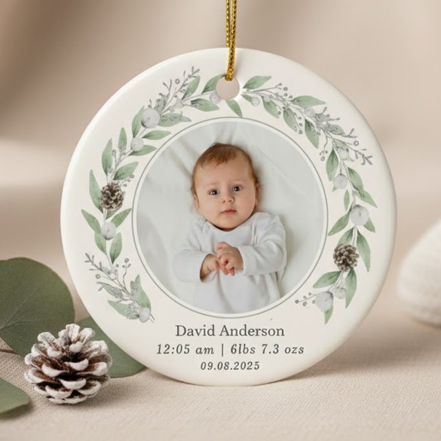 Barns fotopatandag jul 2025 julgransprydnad keramik (A round ornament featuring a central baby photo circled by a delicate watercolor greenery wreath.)