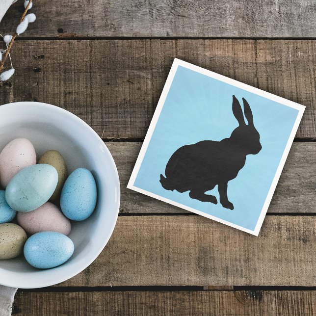 Black Bunny Silhouette Form Tall Öron på Blue Pappersservett (Sitting black silhouette bunny rabbit on blue paper napkin for Easter or spring time.)