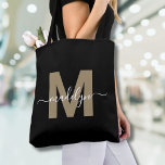 Black Guld Trendig Modern Script Namn Monogram Tygkasse<br><div class="desc">Personlig Elegant Black Guld Trendig Modern Script Namn Monogram Tote Bag. Lägg till en gnutta glöd och sofistikering i stil med den här chicen i väskan. Med en elegant inledande guld (observera: guld är ett platt färg, utan shimmer eller folie) centrerat på en skarp svart bakgrund, och en ren, modern...</div>