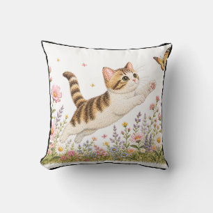 Broderad kattunge jagar fjäril i vildblomma kudde