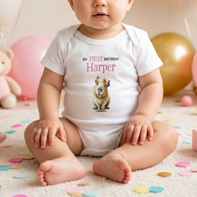 Capybara First Birthday • Birthday Outfit T Shirt (baby wearing white bodysuit with cute capybara and pink first birthday name print on soft floor)