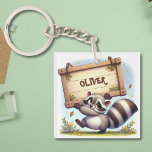 Cute Raccoon med Anpassade Namn Sign<br><div class="desc">Den här lekande personligens nyckelkedja för barn har en söt kapplöpning med en överdimensionerad träskylt namn. Med ett flytande svan som flödar ut för jämvikt,  en fot lyft mitt i tummen,  är denna förtjusande utformning perfekt för personanpassning.</div>