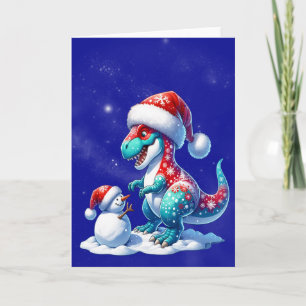 Dinosaur med tomteluva bygger en snöman helgkort