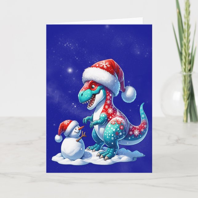 Dinosaur with santa hat building a snowman helgkort (Framsida)