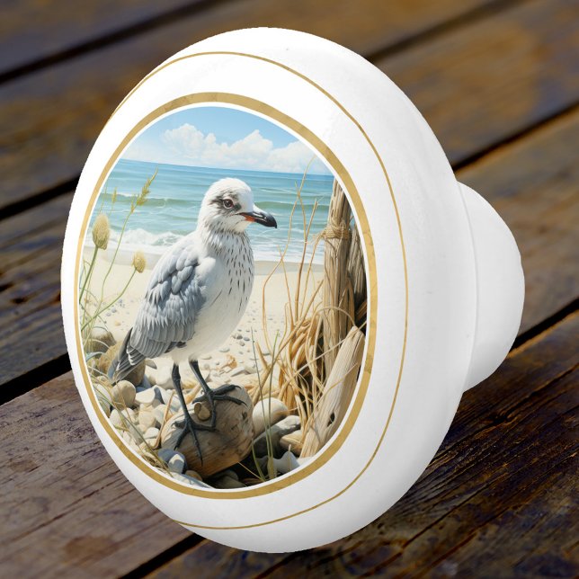 Elegant Fiskmås Beach-kusten Knopp (An elegant ceramic door knob featuring a young seagull at the beach with a gold stylized lining)