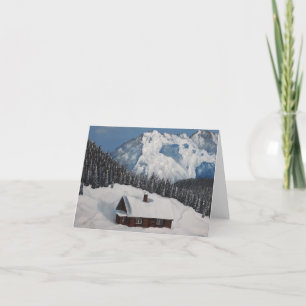 En mysigt vinterstuga, snöberg och skog helgkort