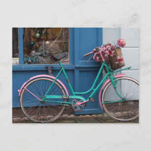 En rosa cykel med korgvide basket och blommor vykort