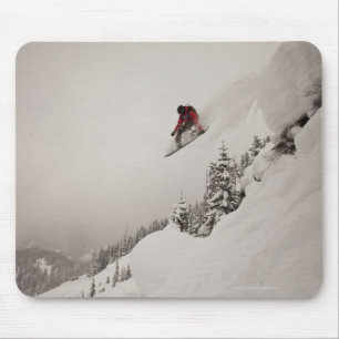 En snowboarder hoppar av en klippa in i pudrar in musmatta