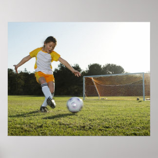 En ung flicka som spelar fotboll på en fotboll fäl poster