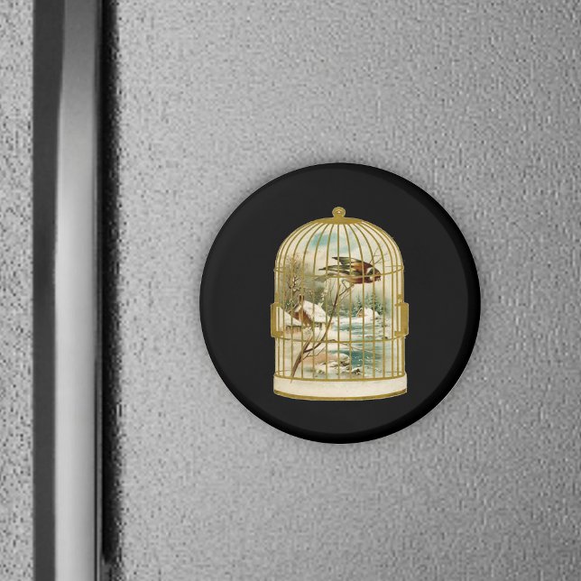 Fågel i burarnas vinterscen magnet (Golden birdcage with winter cabin scene inside bird on branch on black round magnet.)