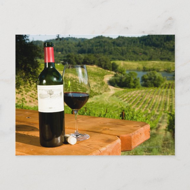 Flaska i rött vin och glas på bord vykort (Framsida)