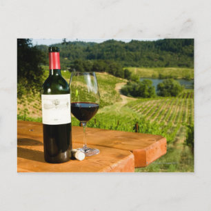 Flaska i rött vin och glas på bord vykort