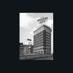 Foto för western automatisk signering av svartvitt canvastryck<br><div class="desc">Vid ovanlig halvcylinderns byggnad dominerar ett Westernt autotecken skylten. Eftersom tecknet inte är parallellt med tegelkonstruktionens platta sida fäster det uppmärksamheten på konstruktionens böjda utformning. En dekorativ betongrälsvinkel över förgrunden som börjar i det nedre lämnat hörnet av ram. Förutom några mycket kortare byggnad till lämnad om Westerna Auto-torn är himlar...</div>