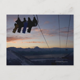 Fyra snowboarders silhuetteras på en skidor hiss vykort