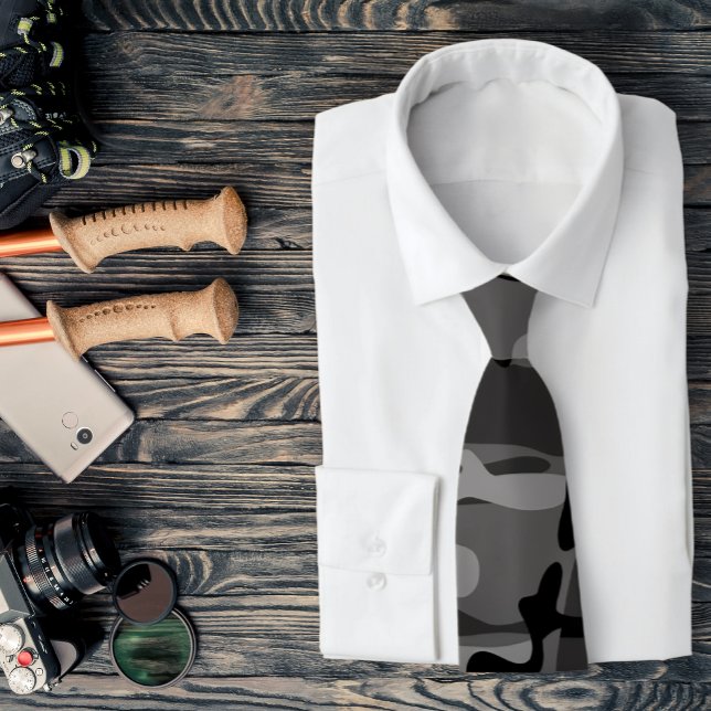 Grå och svart kamouflage slips (A gray camo necktie is featured on a shirt and a assemblage of outdoors related accessories.)