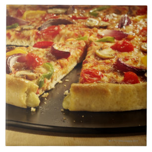 Grönsakpizza som skivas på svart, panorerar på  kakelplatta