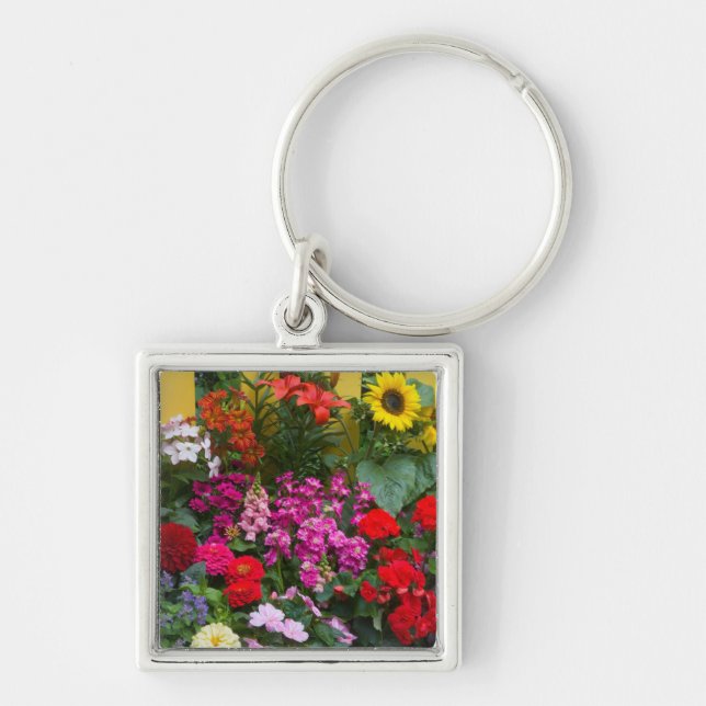 Gul staket med blomsterträdgård framför fyrkantig silverfärgad nyckelring (Framsidan)