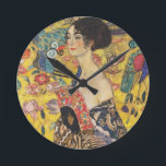 Gustav Klimt dam med fläktart nouveaumålning Rund Klocka<br><div class="desc">Gustav Klimt dam med fläktart nouveaumålning Detta halva porträtt av en härlig kvinna visar en gul bakgrund med asiatic prydnadar, färgrika fåglar, och lotusblomma blommar. Damen ha på sig en klänning i stilen av en kimono imprinted med bevekelsegrunder av en kinesisk drakeklänning. Härlig konstnärlig romantisk dekorativ konstmålning. Se mer av...</div>