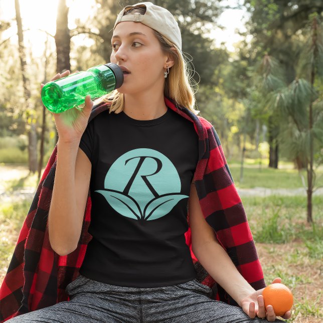 Ikonen Rejuvenescents - Body Care Brand T Shirt (Young woman wears a black shirt with the Rejuvenescents "R" leaf logo. She sips water, holds orange.)