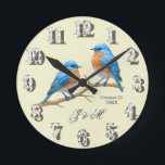 Ivory Pastel Lovebird Romantic Bluebirds Bröllop Rund Klocka<br><div class="desc">Fira din kärlek-historia med detta romantiska bröllop-kort som har en graverande elfenbensbakgrund, en av de trendande pastellttonerna för 2025. Den milda nyansen skapar en elegans och en värme, medan ett par charmerande bluebirds på gren lägger till en naturinspirerad symbol för harmoni och hängivenhet. Förfinad gyllene manustypografi framhäver parets namn, ge...</div>
