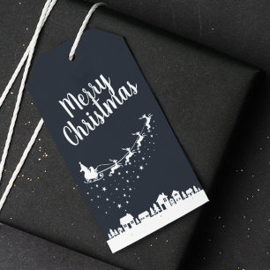 Jultomten med slift och renar ovanför husen presentetikett