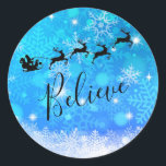 Jultomten och hans flygande renar - tro runt klistermärke<br><div class="desc">Julklistermärken med en svart silhuett av tomten i sitt sligh som dras av hans renar som flyger över himlar. Tro skrivet i ett trendig-skriptteckensnitt. Bakgrunden är en isig blå,  frostig snöflingdesign.</div>