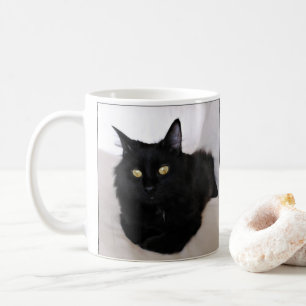 Långhårigare svart katt på soffan kaffemugg