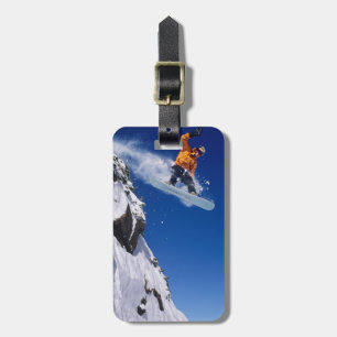 Man på en snowboard som hoppar av en snööverhängan bagagebricka