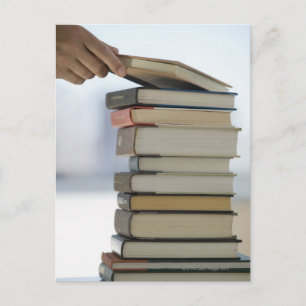 Man's hand taking a book from a stack of books vykort