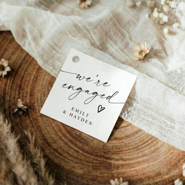 Modern enkel förlovningsfest handskriven hjärta gåvor etiketter (Modern black and white we're engaged favor tags with elegant handwriting and heart)