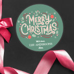 Modern festlig söt grönt och vit God jul Runt Klistermärke<br><div class="desc">Fira helgdagarna i stil med detta moderna klistermärke som har en grönt bakgrund och en glad vit och röd typografi. "God jul"-meddelandet läggs till med holly, snöflingor och baubles och skapar en lekfull men elegant-design. Anpassade med din familj namn och år är det här klistermärket perfekten för att ge helgdagskort,...</div>