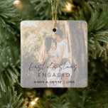 Modern, modern, sensationell skript julgransprydnad keramik<br><div class="desc">Modern julfest med en enkel design med "vår första julklapp engagerad" i en rustik stil-skripttypografi tillsammans med namn och år över ditt favoritfoto med ett ogenomskinligt överlägg. Övertäckningen kan tas bort i designredigeringsverktyget i verktyg. Den här elegantens prydnadsföremål ger en underbar gåva till ett nyligen engagerat par.</div>