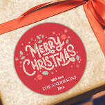 Modern söt och vit God jul Runt Klistermärke<br><div class="desc">Fira helgdagarna i stil med detta moderna klistermärke som har en ljusröd bakgrund och glad vit och röd typografi. "God jul"-meddelandet läggs till med holly, snöflingor och baubles och skapar en lekfull men elegant-design. Anpassade med din familj namn och år är det här klistermärket perfekten för att ge helgdagskort, gåvor...</div>