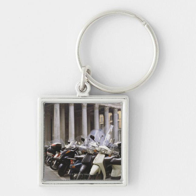 Motoriska sparkcyklar som in parkeras utanför fyrkantig silverfärgad nyckelring (Framsidan)
