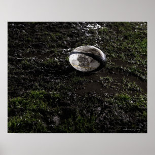 Muddy rugby boll sitta på ett tuggat gräs poster