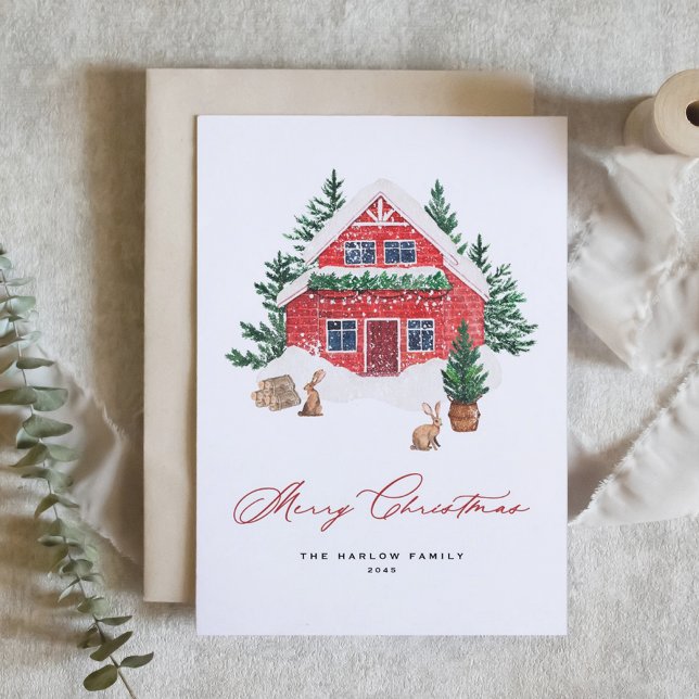 Mysiga vattenfärgsröd julstuga Rustic Helgkort (Christmas card featuring a red cottage tucked in a snowy landscape with fir trees and rabbits.)