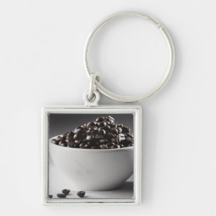 Närbild av en bunkefullt av kaffebönor fyrkantig silverfärgad nyckelring