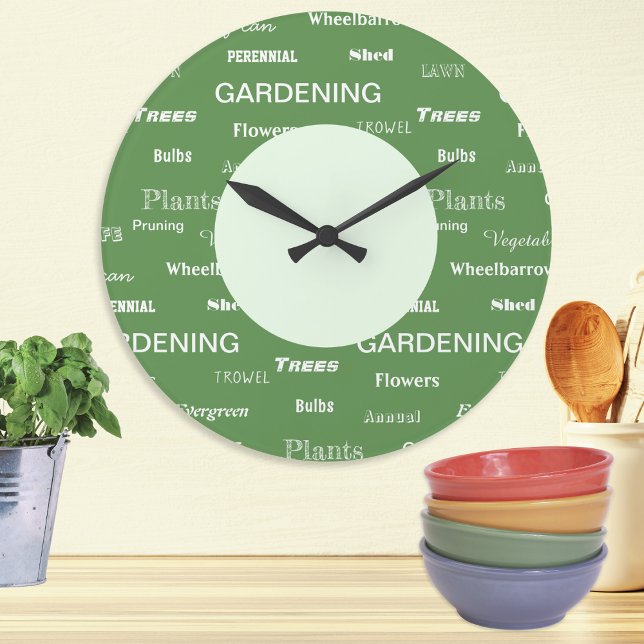  Ord Garden Thétes Patternated Grönt Stor Klocka (A stylish wall clock with gardening themed words in a repeat pattern, in white on green)