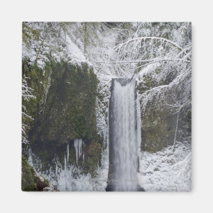 Oskarp vattenfall som omges av en snöig skog magnet