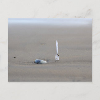 plastgaffel som fastnar i sandig strand bredvid vykort