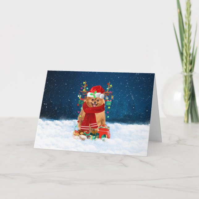 Pomeranian hund i snö med julklappar kort (Framsida)
