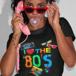 Retro I Kärlek 80-talet | 80 T Shirt<br><div class="desc">Roligt och färgstark 80-talets svarta t-shirt med ljus neon-färgad text som säger "i kärlek på 80-talet",  ett kassettband,  ljusa retrosolglasögon,  ett ghettoblaster (boombox) och några spridda stjärnor.</div>