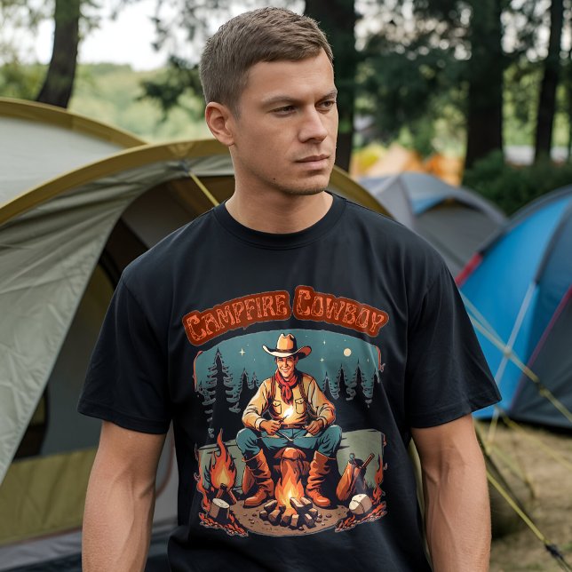 Retro lägereld cowboy västlig grafik t shirt (A man wearing a black t-shirt with a "Campfire Cowboy" graphic design, standing in front of a camp)