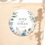 Rustic Boho Dusty Blåa blommor Bröllop Runt Klistermärke<br><div class="desc">Vi presenterar vår Personlig Bröllop Sticker, en harmonisk blandning av rustik och contemporary elegans. Denna vackert utformade dekal har en charmerande vattenfärgandekrans som visar en känslig arrangemang av neutralt och dammigt blåa blommor. I blommigtens hjärta är namn elegant inskrivet i ett klassiskt serif-teckensnitt, sömlöst sammankopplat av "Och" i ord i...</div>