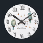 Rustic Woodland Love birds Romantic Bröllop Rund Klocka<br><div class="desc">Den här charmerande bilden har två ömtåliga fåglar som är placerade på en bare gren, omgivna av hängglas ljus som ser ut som vintage lyktor. Fågelfjädrarnas mjuka nyanser av grönt och blått och den minimalistiska bakgrunden ge ger en vismisk och rustik känsla. Ljus tillför en varm, magisk glöd, skapar scenen...</div>